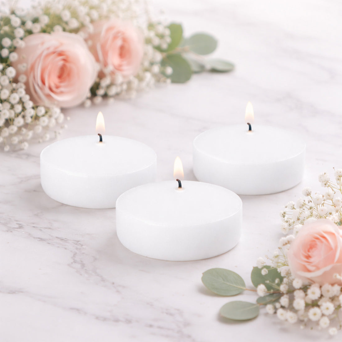 Three white candles lit, surrounded by pink roses and greenery.