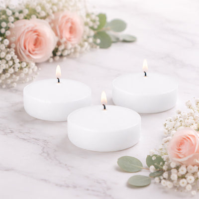 Three white candles lit, surrounded by pink roses and greenery.