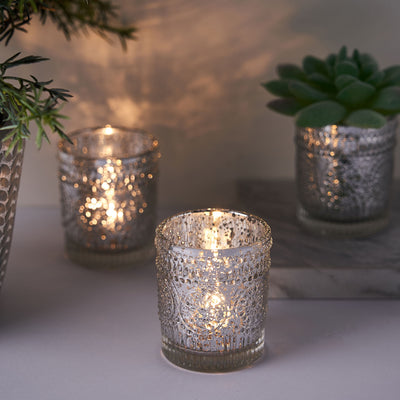 Decorative glass candle holders with warm glowing lights and greenery