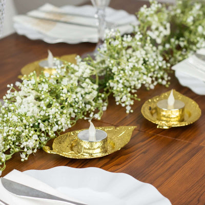 Gold leaf candle holders with white flowers on a wooden table setting.