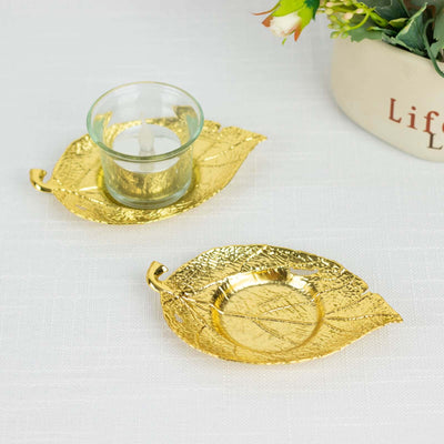 Gold leaf candle holder set with glass votive on a decorative white surface.