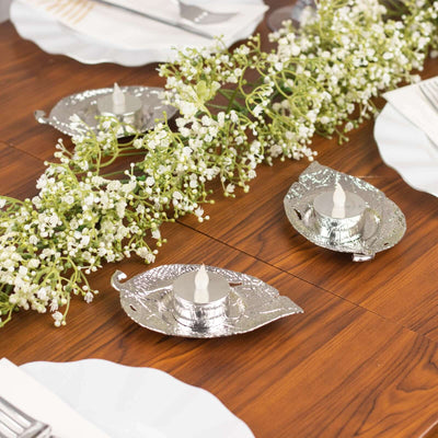 Decorative silver leaf candle holders on a wooden table with greenery.