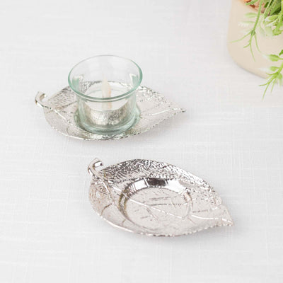 Silver leaf-shaped candle holder and glass votive on a white surface.