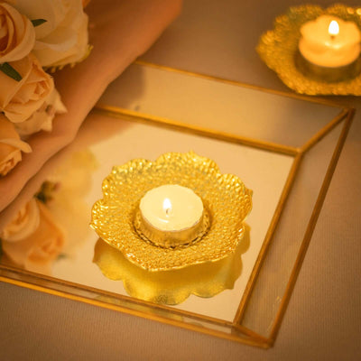 Tea light candle in a decorative gold holder on a reflective tray with roses.