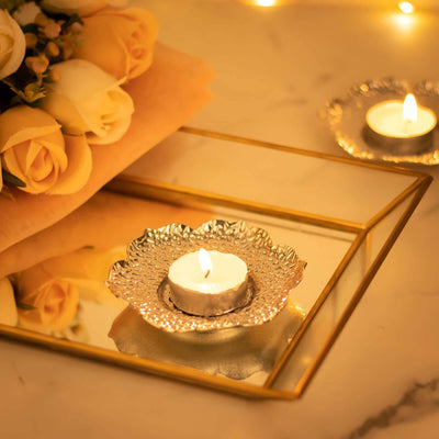Elegant candle in silver holder on reflective tray with roses in background.