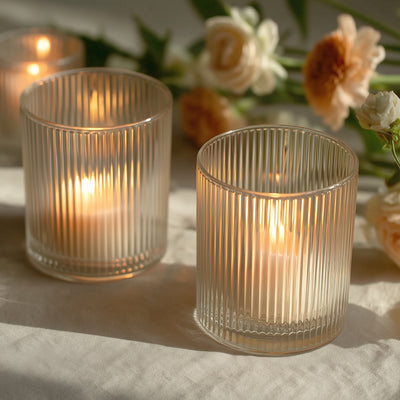 Elegant ribbed glass candles with warm, glowing flames and delicate flowers in the background.