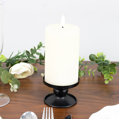 White pillar candle in black holder with greenery on wooden table.