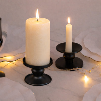 Two elegant candles with black holders on a soft surface, softly lit with fairy lights.