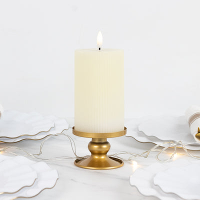 Cream pillar candle on a gold holder, surrounded by elegant white plates and fairy lights.