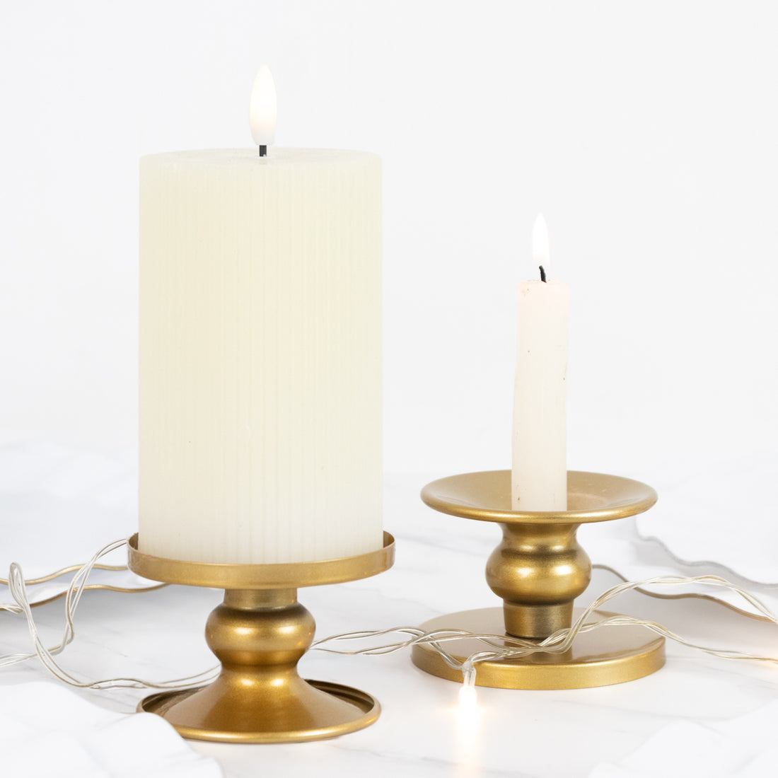 White pillar candle and gold candle holder on a plain background.