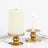 White pillar candle and gold candle holder on a plain background.
