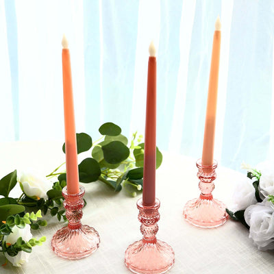 Three elegant tapered candles in decorative holders on a table with greenery and flowers.