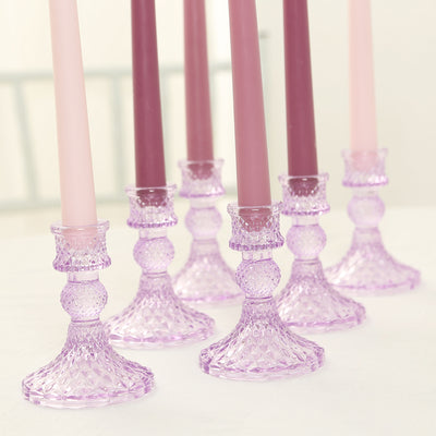 Purple glass candle holders with tapered candles in various shades.