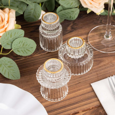 Three elegant glass candle holders with gold accents on a wooden table.