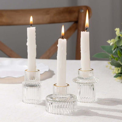 Three elegant glass candle holders with white candles, lit and styled on a table.