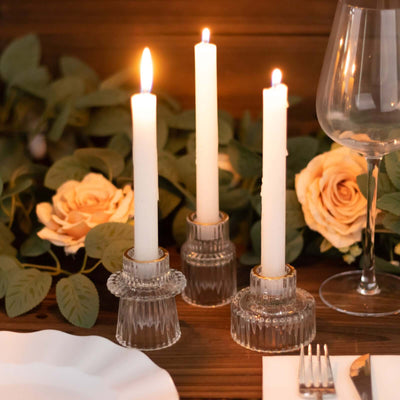 Elegant glass candle holders with white candles and roses on a wooden table.