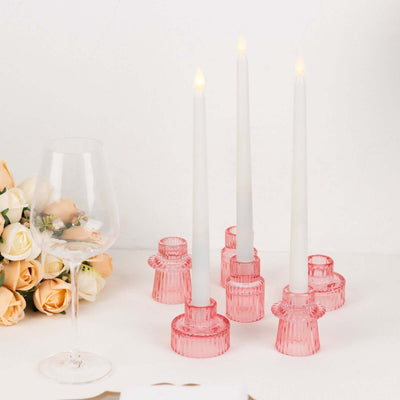 Pink candle holders with white candles and a glass beside a bouquet of roses.