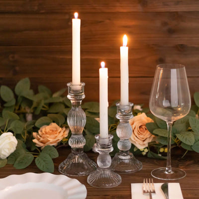 Elegant glass candle holders with lit candles and a wine glass on a rustic table.