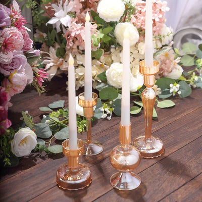 Elegant glass candle holders with white candles and floral backdrop.
