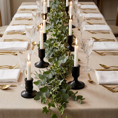 Elegant candlelit dining table with greenery, gold cutlery, and crystal glasses