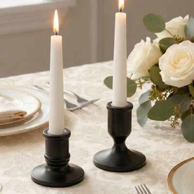 Elegant black candle holders with lit taper candles and white roses on a table.