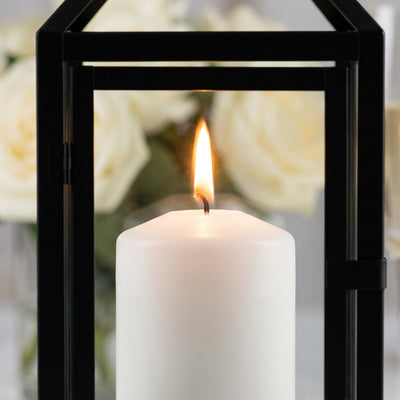 Lit white candle in black lantern with blurred floral background