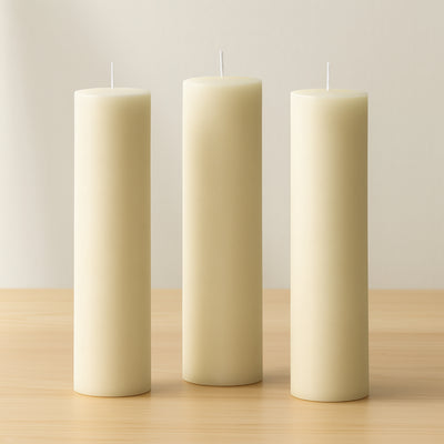Three tall cream-colored candles on a wooden surface.