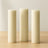 Three tall cream-colored candles on a wooden surface.