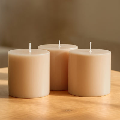 Three beige pillar candles on a wooden surface.