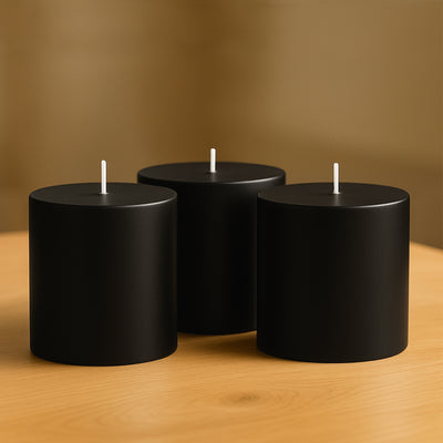 Three black cylindrical candles on a wooden table.