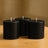 Three black cylindrical candles on a wooden table.