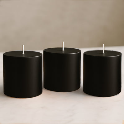 Set of three black cylindrical candles on a marble surface.