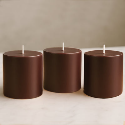 Set of three brown cylindrical candles on a light surface.