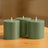 Set of three green cylindrical candles on a wooden surface.