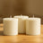 Three ivory pillar candles on a wooden table.
