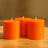 Three vibrant orange candles displayed on a wooden table.