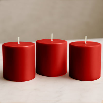 Set of three red pillar candles on a neutral surface.