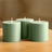 Three green cylindrical candles on a wooden table.