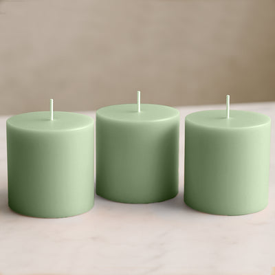 Three green pillar candles on a soft surface.