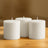 Set of three white candles on a wooden table.