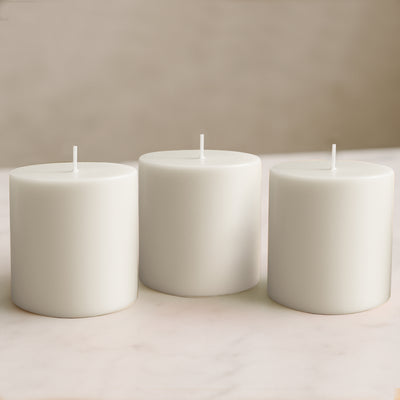 White pillar candles in varying heights on a neutral surface.