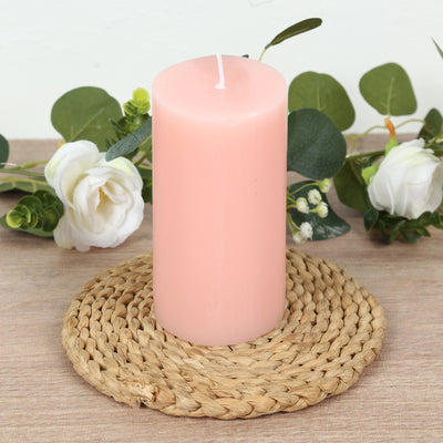 Pink pillar candle on a woven coaster with decorative greenery.