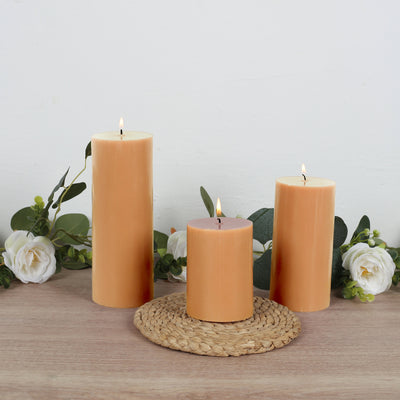Three orange pillar candles with white roses on a woven mat.