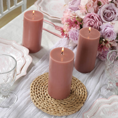 Pink pillar candles on a table with flowers and glassware.