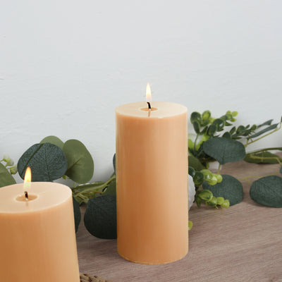 Orange pillar candles with greenery decor on a wooden surface.