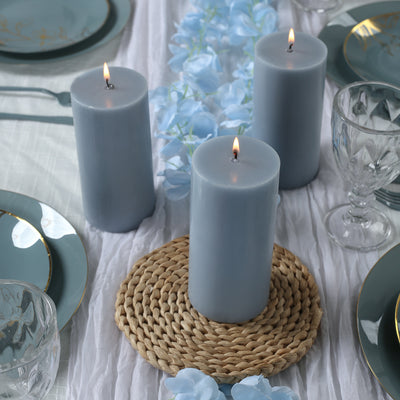 Gray pillar candles on a table setting with blue accents and decorative flowers.
