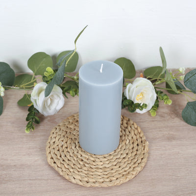 Gray pillar candle displayed on a braided mat with greenery and flowers.