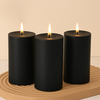 Black cylindrical candles with flames on a wooden tray.