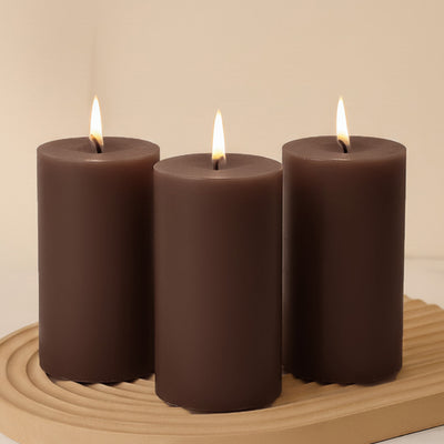 Set of three brown pillar candles with flames, arranged on a wooden tray.