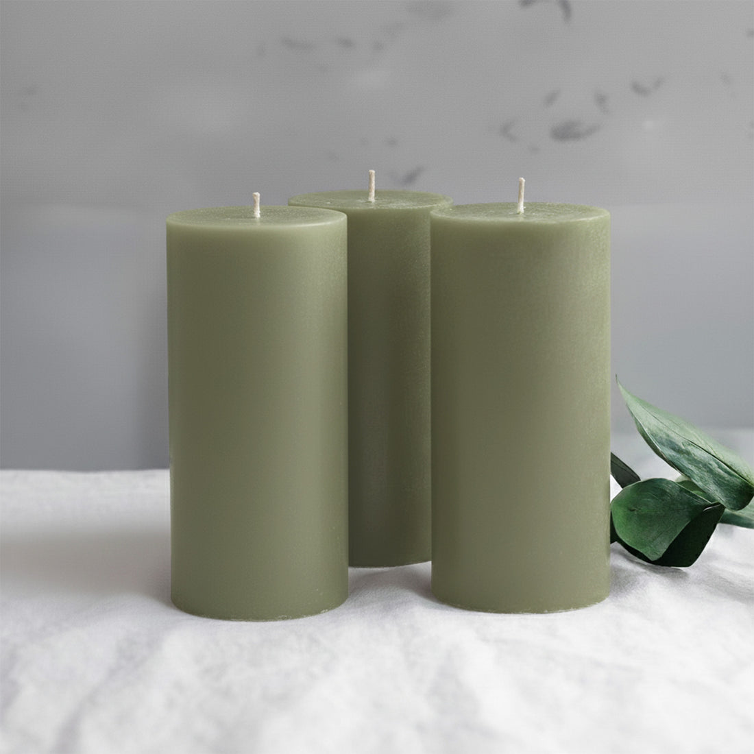 Three green pillar candles with a leaf accent on a soft surface.